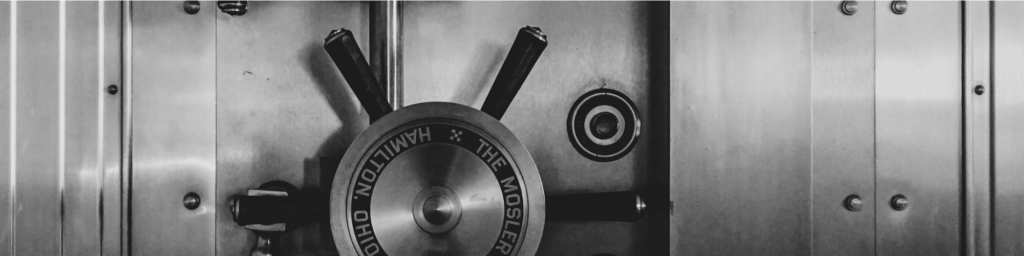Grey scale photo of a big old style safe, with the turning wheel on the left hand side of the picture