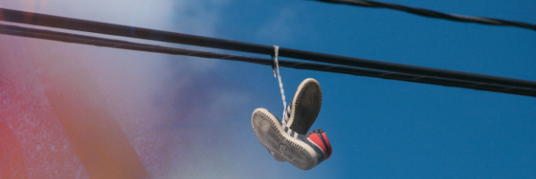 A paid of red shoes with a while soles with tied shoe laces hanging over powerlines against a clear blue sky