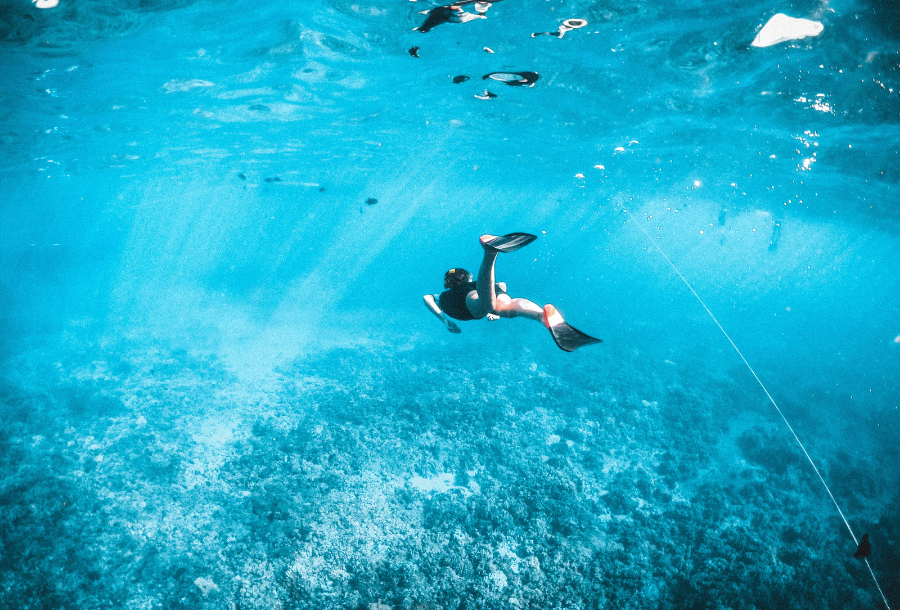 An open beautiful underwater shot of a girl swimming off into the distance in crystal clear water, wearing flippers with sun beams shining through