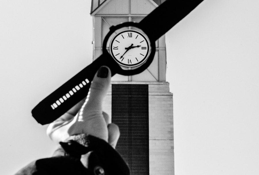 Black and white picture of a hand being held up golding a watch over the face of a white clock tower in the background.