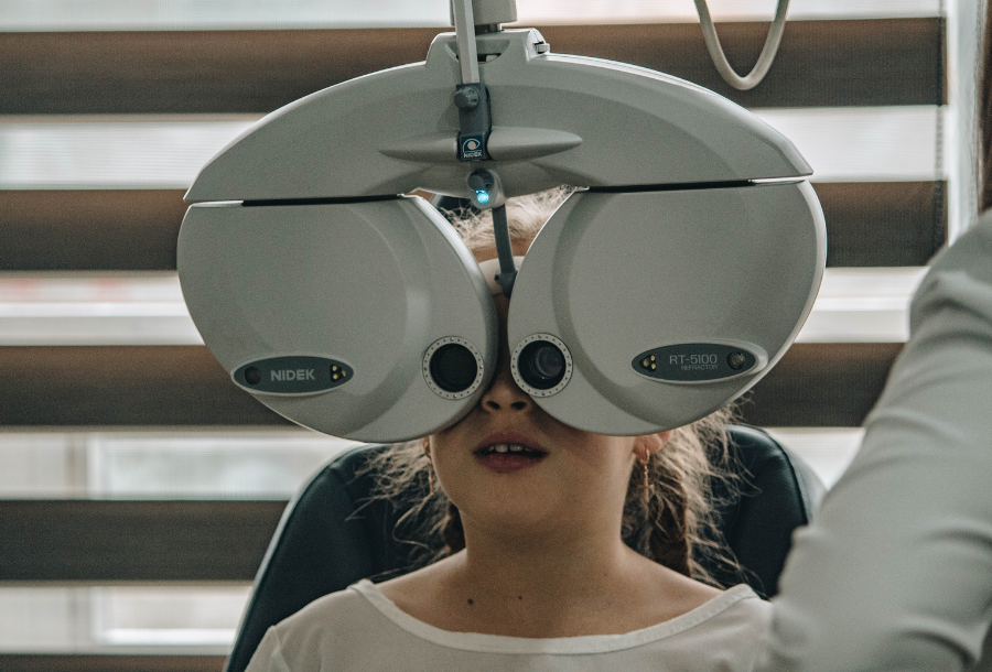 Primary school aged girl wearing a white round neck t-shirt having her eyes tested at the optometrist
