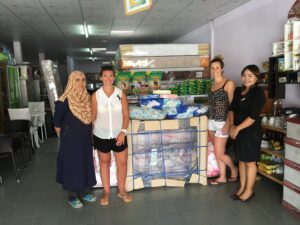 Phoebe Wilkens and Donna Lindsay standing on either side of bedding equipment standing side by side a Thai Special Education School teacher with a donation of bedding goods for the school