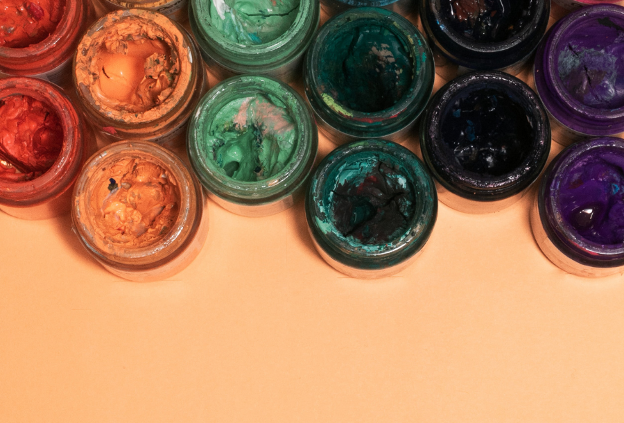 left to right; beautiful rich paint pots full of red, orange, green, emerald green, black and rich purple on a muted orange background