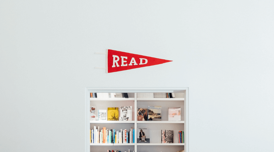 Pictured a small entry to a hole in the wall type bookshelf filled with lots of different books, above the entrance is a red triangle flag that says "READ"