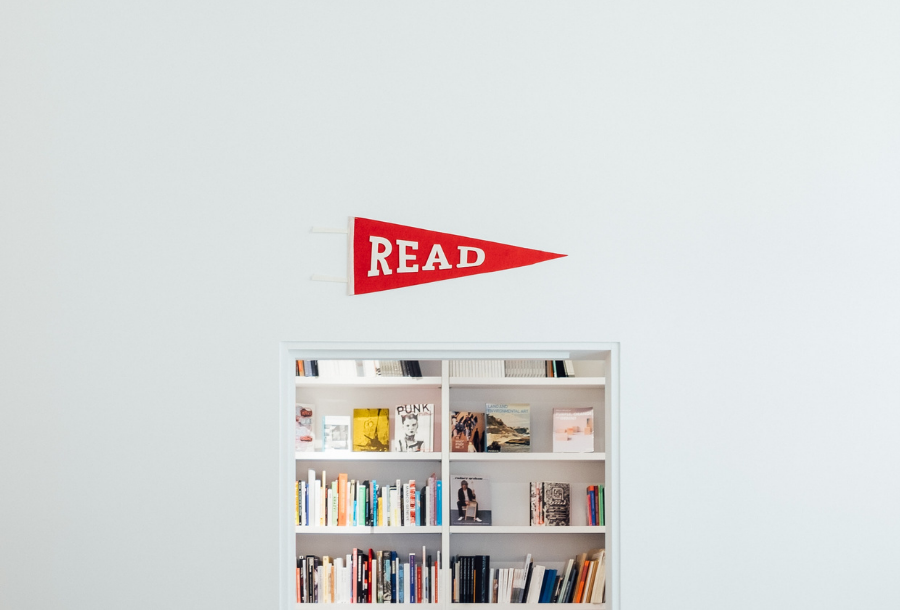 Pictured a small entry to a hole in the wall type bookshelf filled with lots of different books, above the entrance is a red triangle flag that says "READ"