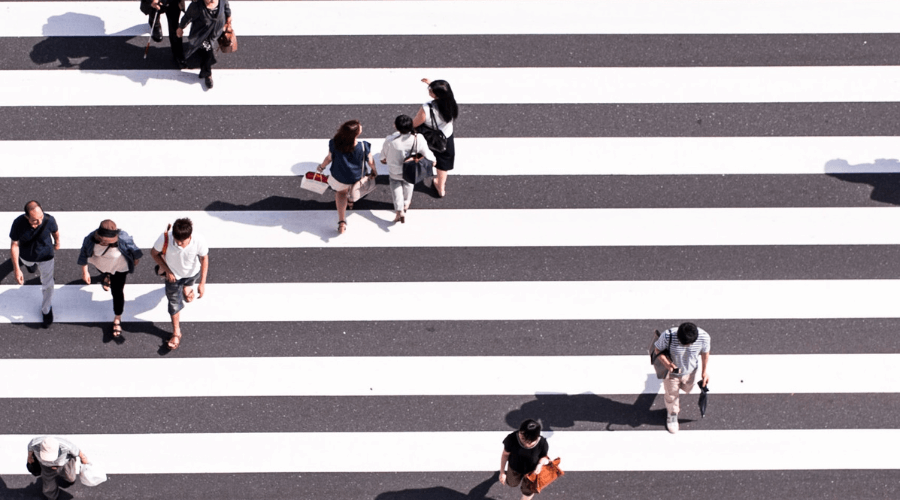 Birds eye view of a street crossing, white stripes over the road with people walking in different directions to cross the road