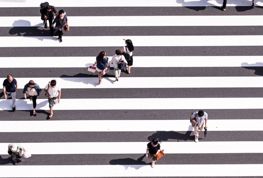 Birds eye view of a street crossing, white stripes over the road with people walking in different directions to cross the road