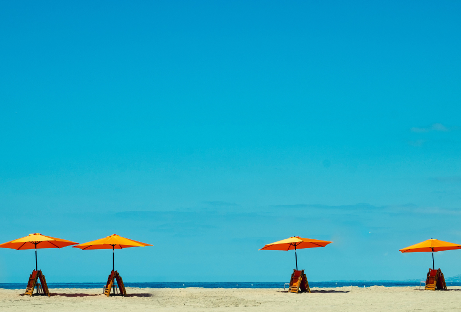 Beautiful clear blue skies with soft sand and four wooden beach chairs and umbrellas in the distance, both a striking orange colour