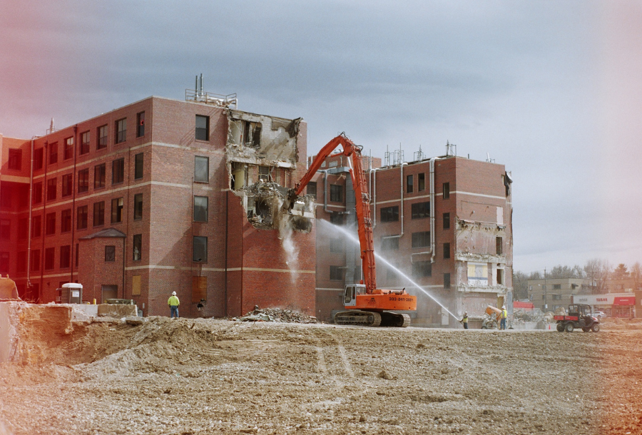 Pictured, a crane breaking down a brick building with a lower water gun keeping the dust at bay