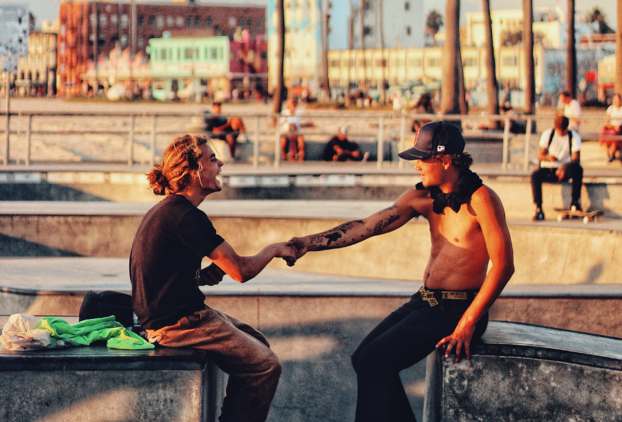 Pictured, two men sitting down at a skate park in the afternoon sun shaking hands and having a laugh