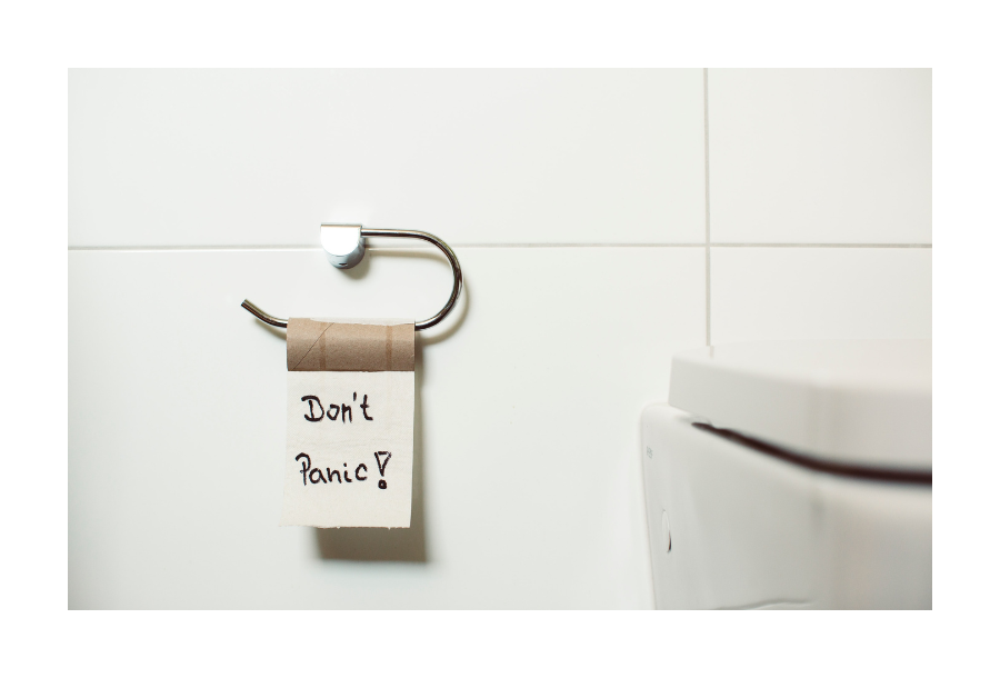 Pictured, a closed white toilet seat, sitting next to it is an empty toilet roll with one sheet of toilet paper left and the words "Don't Panic!" written on them in a black marker.