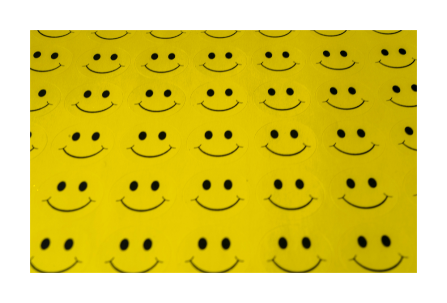 Pictured, a row of bright yellow stickers with smiley faces on them. Two black coloured eyes and a big black coloured mouth in the shape of a smile.