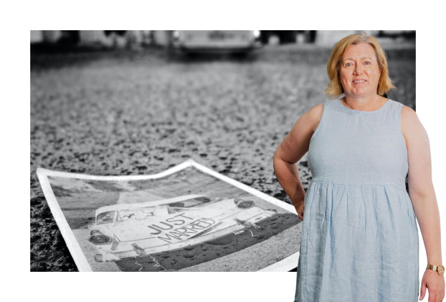 Pictured, Director Krystine Canny-Smith wearing a sleeveless light blue dress and a stock picture behind her with a black and white picture of a wedding car on the road.