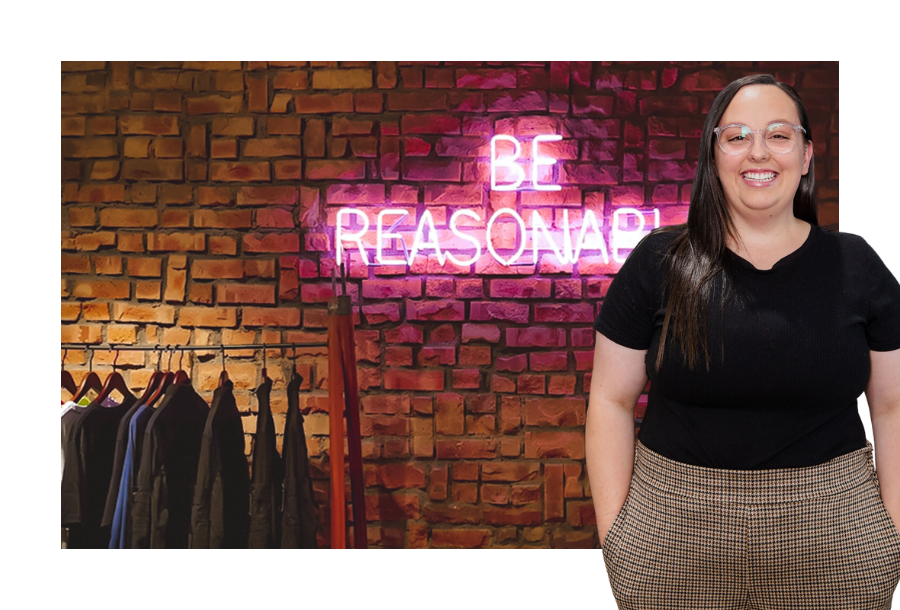 Pictured, NDIS Plan Management team member, Mekayla standing in front of a stock picture of a brick wall with neon lights lit up in pink saying "be reasonable"