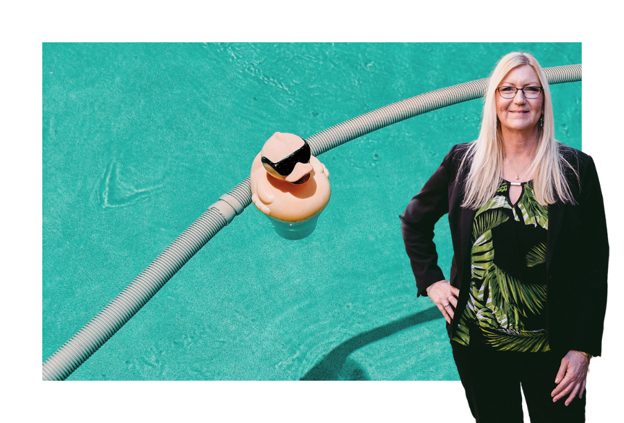 A picture of a yellow rubber ducky with black sunglasses in a swimming pool, standing in front of the picture is Julie Pullen