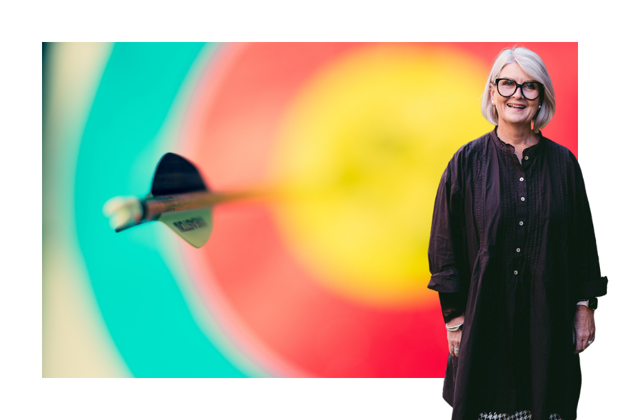 Pictured, Director Amanda Wilkens standing in front of a stock picture of a blurred blue, red and yellow target with a bow pointing out.