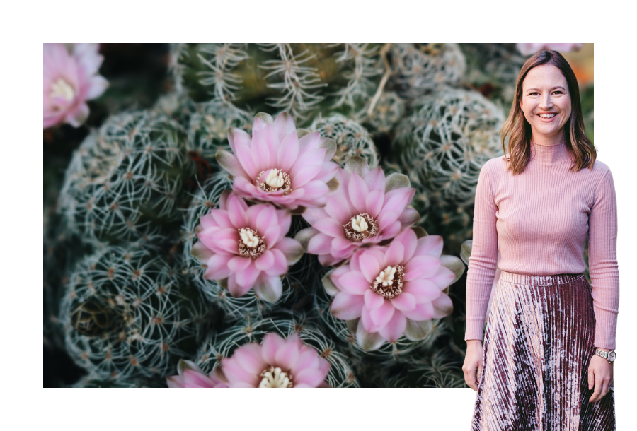 Pictured, Gabrielle Andersen standing in front of a stock picture of green cactuses with purple flowers growing.