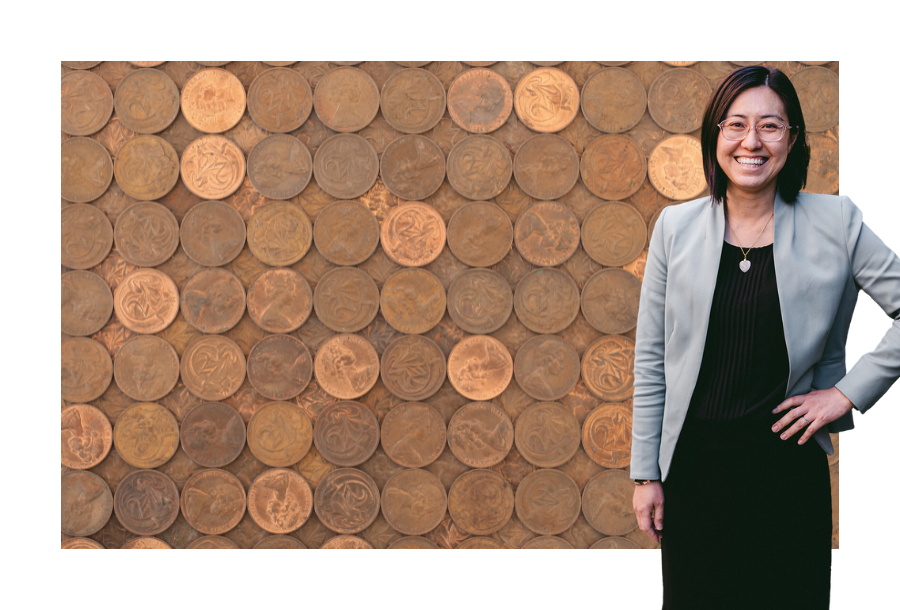 Helen Yau wearing a teal coloured blazer, a black dress with one hand on her hip. Standing in front of a stock picture of Australian two-cent pieces lined up against each other in rows