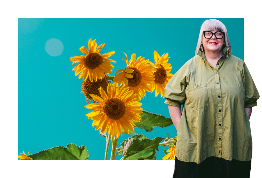 Pictured, a clear blue sky surrounded by bright yellow sunflowers in the centre with Anthea Taylor standing on the right hand side wearing a green top and her hands in her pockets.