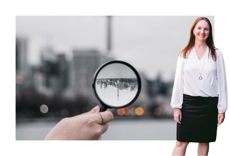 Pictured, Samantha Butcher with her hands by her side, wearing a long sleeve white top, a black pencil skirt and a big smile. In the background is a picture of a hand holding a magnifying class with a picture of a landscape upside down against a gloomy overcast background.