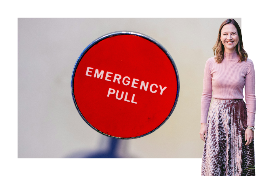 Pictured, Gabrielle Andersen with a big smile on her face wearing a long sleeve ribbed pink skivvy and a long dark pink velvet skirt. In the background is a picture of a muted white background and a big round red button, black outline with the words "EMERGENCY PULL" written in white.