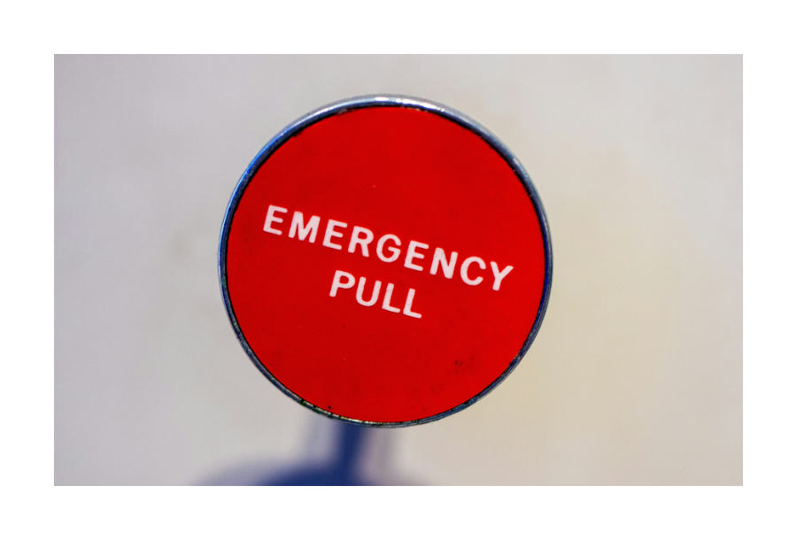 Pictured, a close up view of a red emergency pull button. There is a red button with a black outline, white writing in the middle in capital letters that says "EMERGENCY PULL"