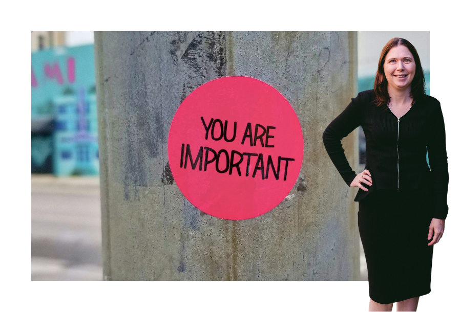Pictured, Karlene Wightman with one hand on her hip and a great big smile on her face. Wearing a long sleeve black dress Karlene stands in front of a power pole, close up with a bright pink circle in the centre of the image, that says in black capital letters "YOU'RE IMPORTANT".