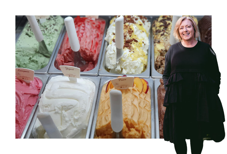 Pictured, Krystine Canny-Smith with a big smile on her face and her hands in her dress pockets. In the background is a close up photo of different flavours of ice-cream looking delicious!