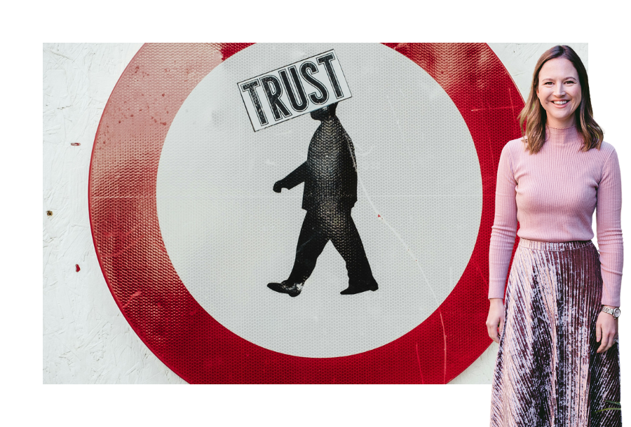 Pictured, Gabrielle Andersen wearing a long pink velvet skirt with a long sleeve pink top and a big smile on her face. In the background is a big red circle and inside on white print is a picture of a spray painted man with the words "trust" covering his face.