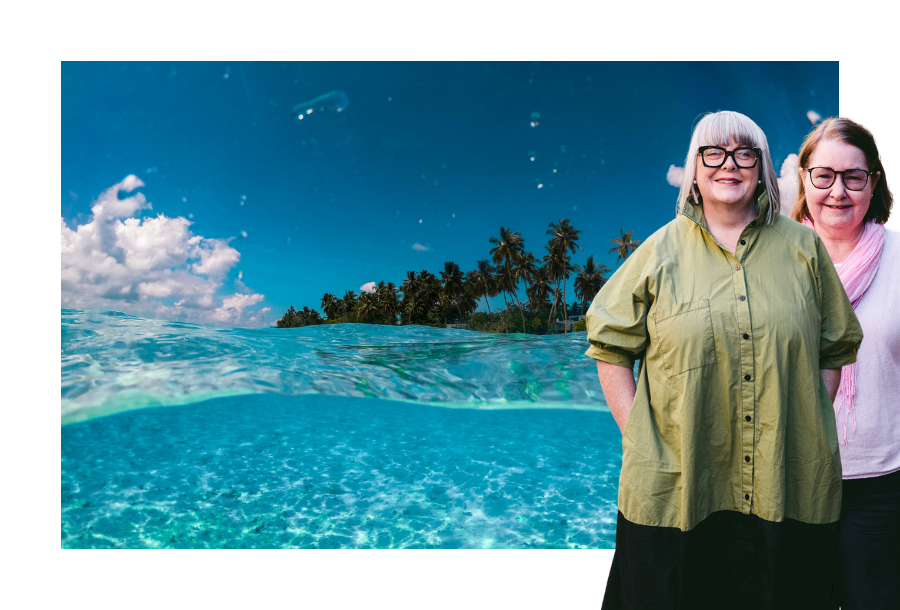 Pictured, Anthea Taylor and Christine Friel, standing in front of a picture of a beautiful blue cleared water beach and sandy shores. There are palm trees in the background and a crystal clear blue sky.