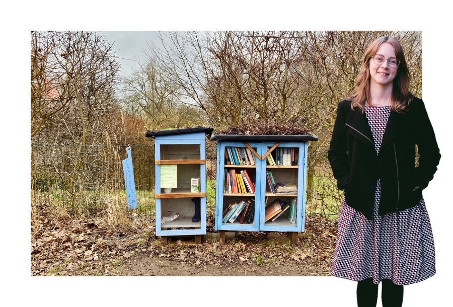 Pictured: Brittany Bell, standing in a colourful dress with a black jacket on, hands in her pockets and smiling. She's standing in front of a light blue public library cabinet that stands on the side of the road.