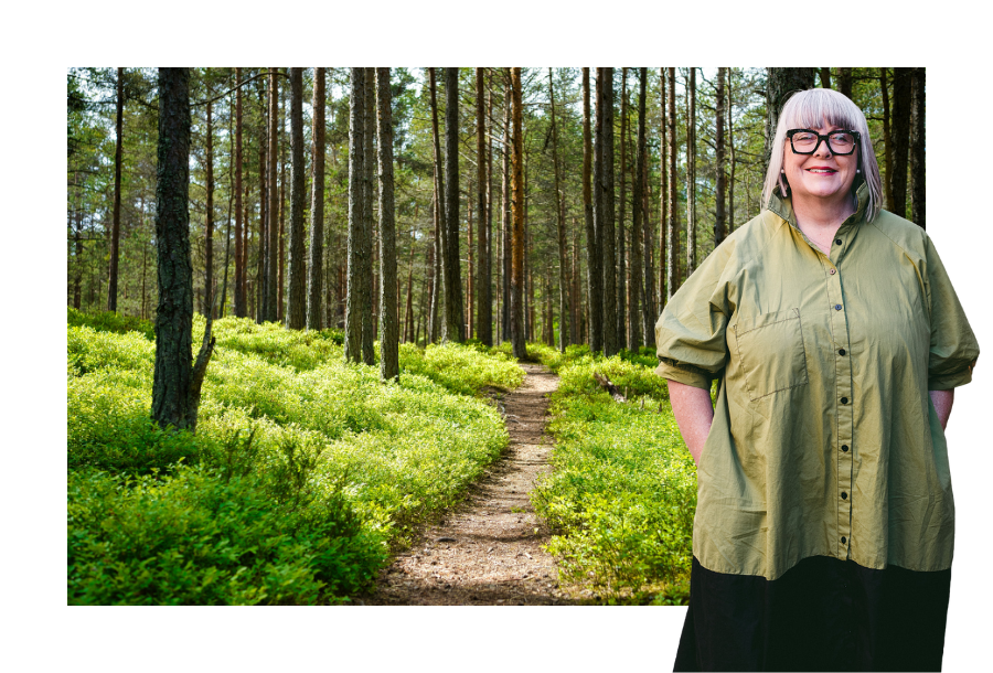 Pictured; Head of Canny Plan Management, Anthea Taylor; standing smiling with her hands in her pockets wearing a long black skirt in a green shirt. Behind her is a photo of a beautiful dirt trail that leads into a bright green forest.