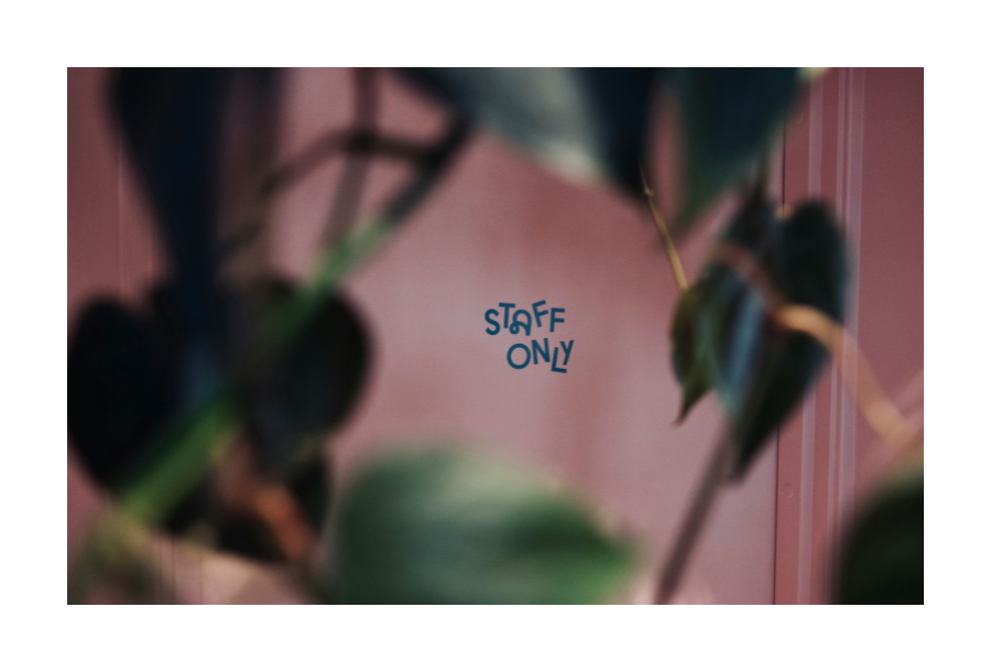 Pictured, a pink coloured doorway and wall with the words written in black writing "staff only" and in the foreground are muted leaves.