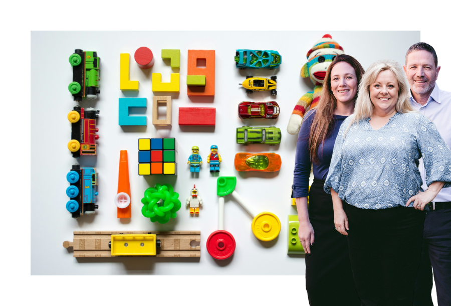 Pictured: Canny Accounting Managers, Jamie, Michelle and Adam standing smiling in front of an image of neatly organised toys in a variety of colours.