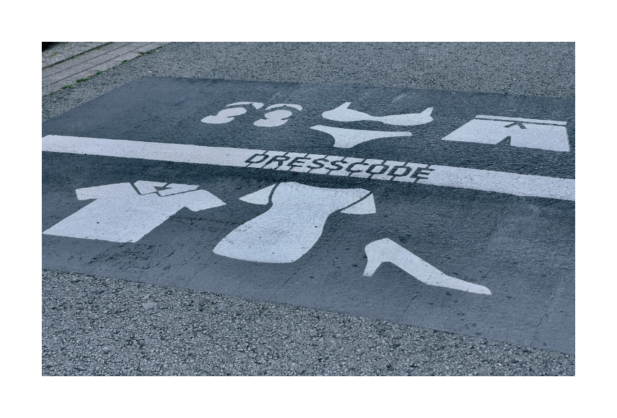 Pictured, a road with a painted plate on it with different while stenciled paintings of clothing and footwear and in the centre the words "DRESS CODE"