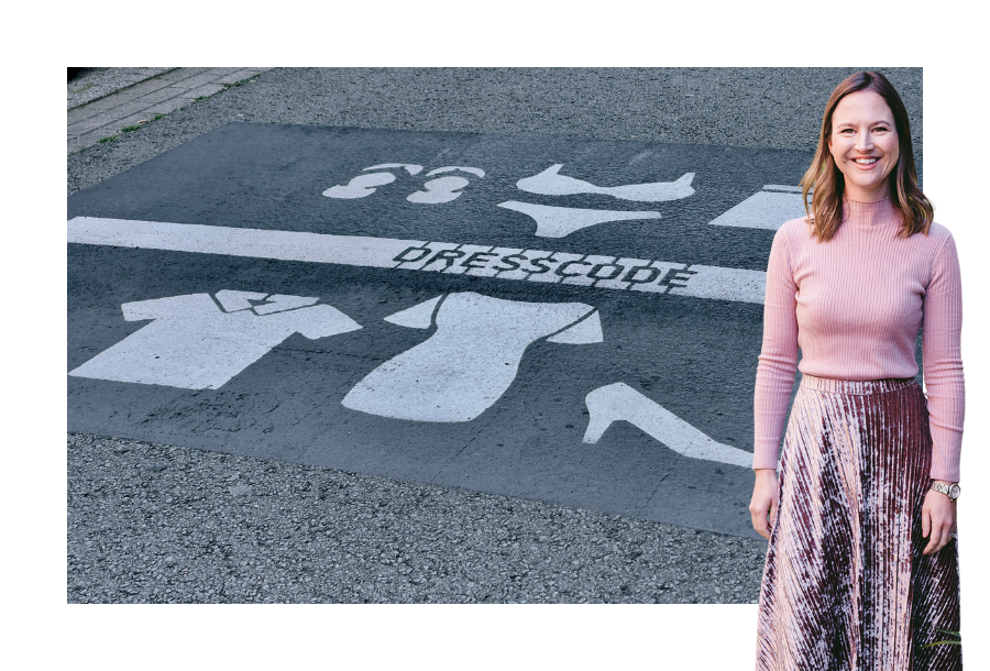 Pictured, Gabrielle Anderson wearing pink on pink with a big smile on her face. In the background is a picture of a road with the words spray painted in white "Dress Code"