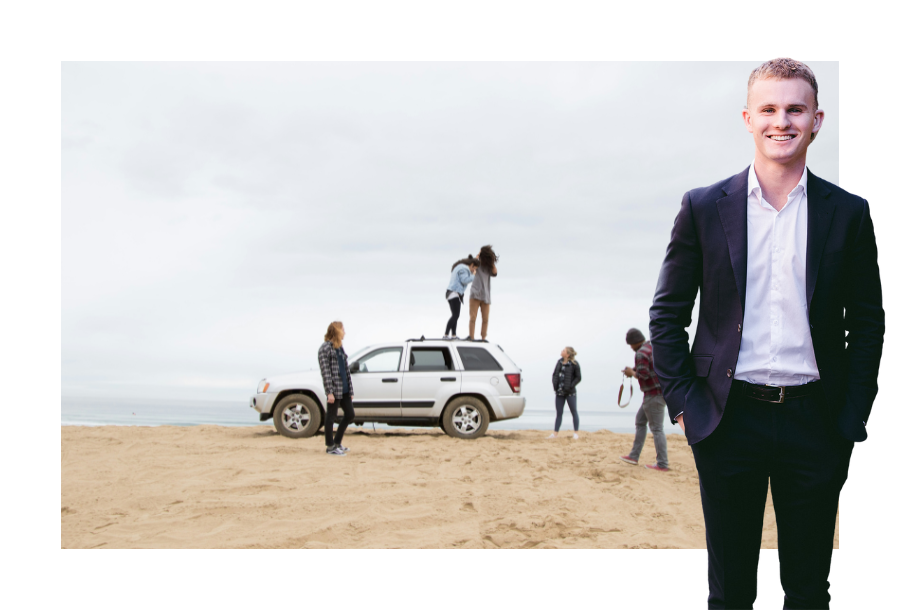 Pictured, Jayden Scott with a big smile on his face and his hands in the pockets of his black suit. In the background is a picture of a white card and younger aged people standing on a beach, some are standing on the top of the car and looking at which direction to go in.