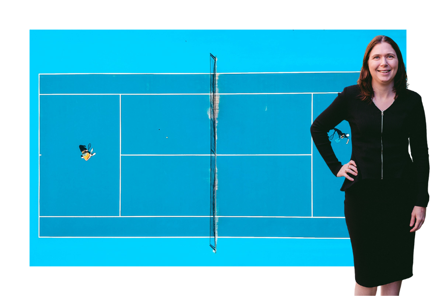 Pictured: Karlene Wightman standing smiling wearing a black skirt and black top. Behind her is a top-down image of two people playing tennis on a blue tennis court.