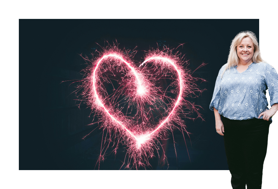 Pictured: Michelle Flowers standing smiling with one hand on her hip in a light blue top and black pants. Behind her is an image of a dark night sky with a love heart made from prink sparks.