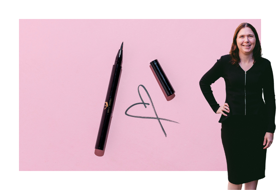 Pictured, Karlene Wightman wearing a black long sleeve dress, one hand on her hip and a big smile on her face. Behind her is an image black marker with a heart drawn next to it on pink paper.