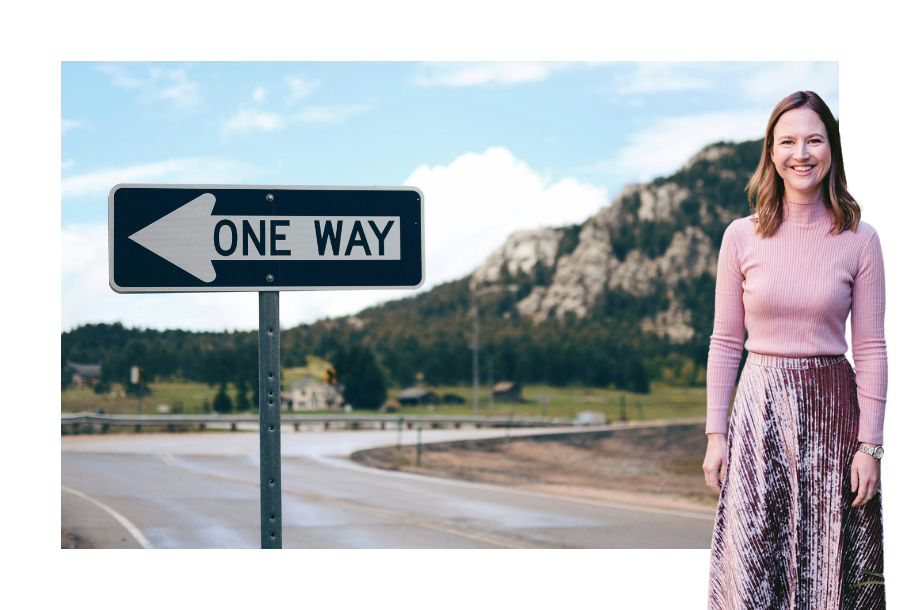 Pictured: Gabrielle Andersen standing smiling wearing a pink long sleeve top and a pink long skirt. Behind her is an image of a road and a sign that reads, "one way".