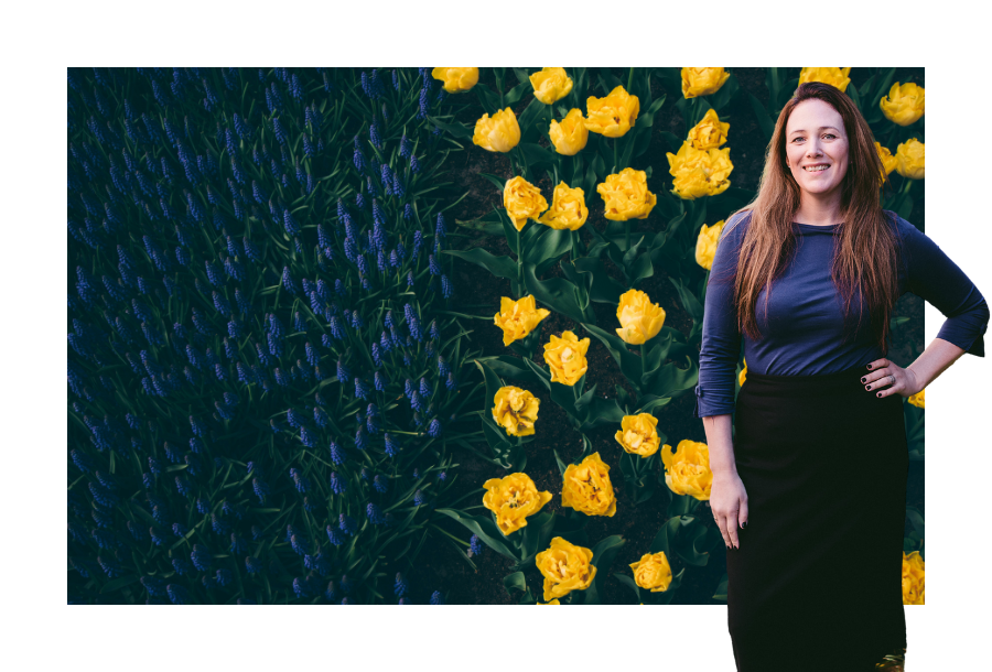 Pictured, Jamie Arrington standing on the right hand side of the picture. In the background is an aerial view of a field of flowers. On the left are deep purple lillies and on the right hand side is bright yellow daffodils